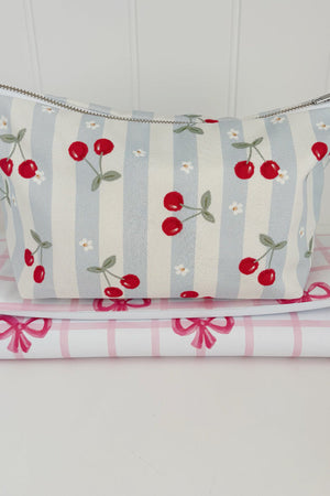 Nappy Wallet Cherry Stripe, front view sitting on top of two folded pink bow gingham changing mats