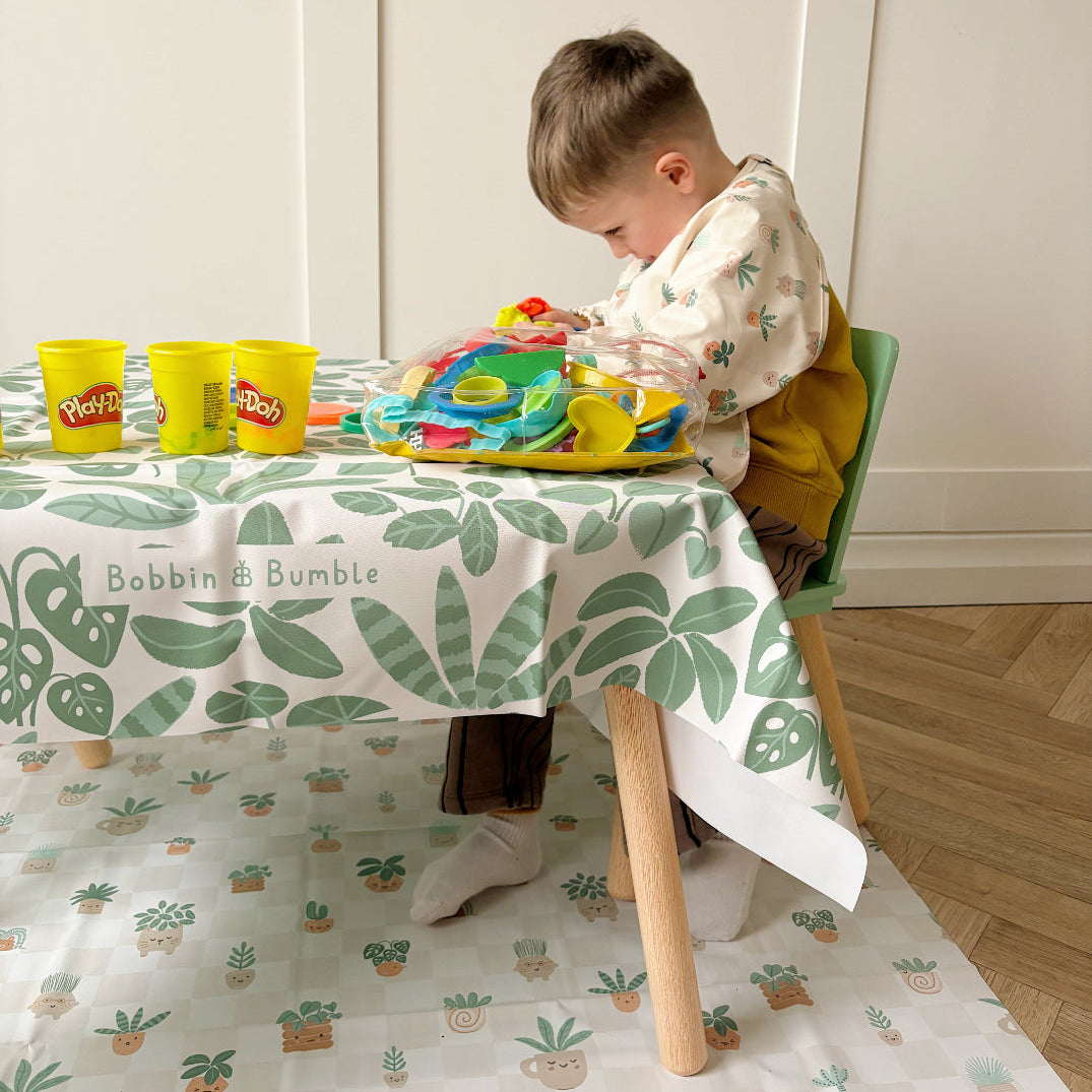 Toddler playing with play dough at a small table, with the Pot Plants splash mat on the floor underneath
