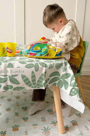 Toddler playing with play dough at a small table, with the Pot Plants splash mat on the floor underneath