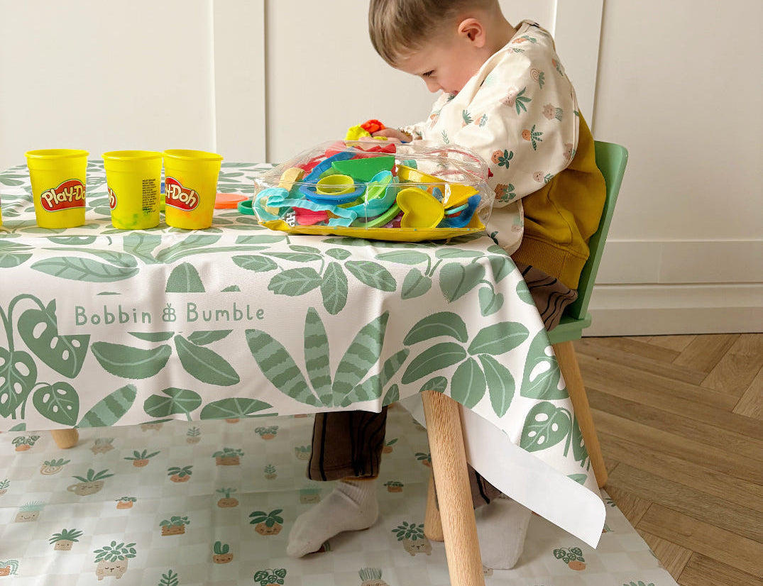 Toddler playing with play dough at a small table, with the Pot Plants splash mat on the floor underneath