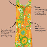 A retro-style maternity dress with a vibrant orange, green, and yellow floral print, shown with text callouts detailing its nursing features and vintage design on a solid tan background.