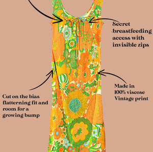 A retro-style maternity dress with a vibrant orange, green, and yellow floral print, shown with text callouts detailing its nursing features and vintage design on a solid tan background.