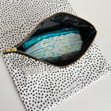 Nappy wallet in dalmatian print, open from above with nappies and a pack of baby wipes inside, on a spotted mat
