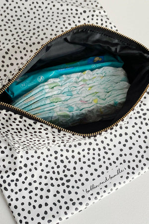 Nappy wallet in dalmatian print, open from above with nappies and a pack of baby wipes inside, on a spotted mat