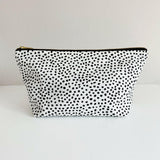 Nappy wallet in dalmatian print, front view of the black spotted white pouch with a gold zip on a plain surface