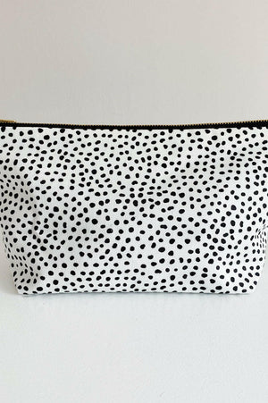 Nappy wallet in dalmatian print, front view of the black spotted white pouch with a gold zip on a plain surface