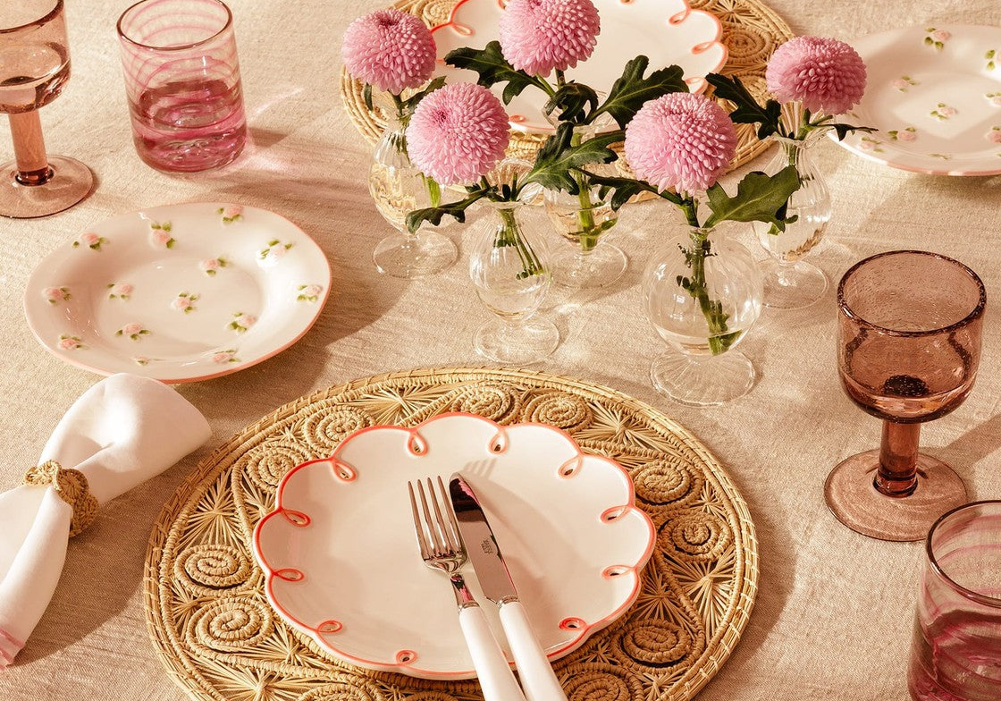 Pretty in Pink Scalloped Lunch Plate on a woven placemat with cutlery, on a table with pink flowers and glasses