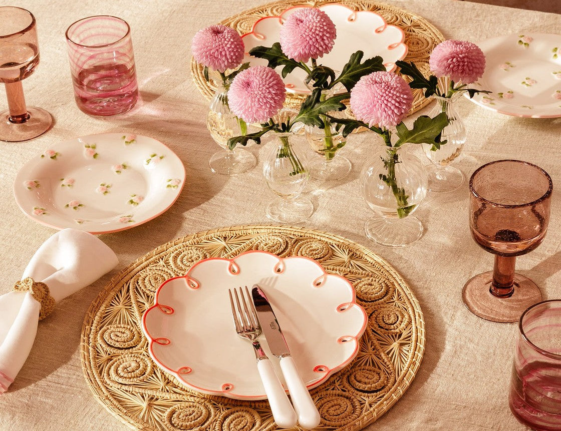 Pretty in Pink Scalloped Lunch Plate on a woven placemat with cutlery, on a table with pink flowers and glasses