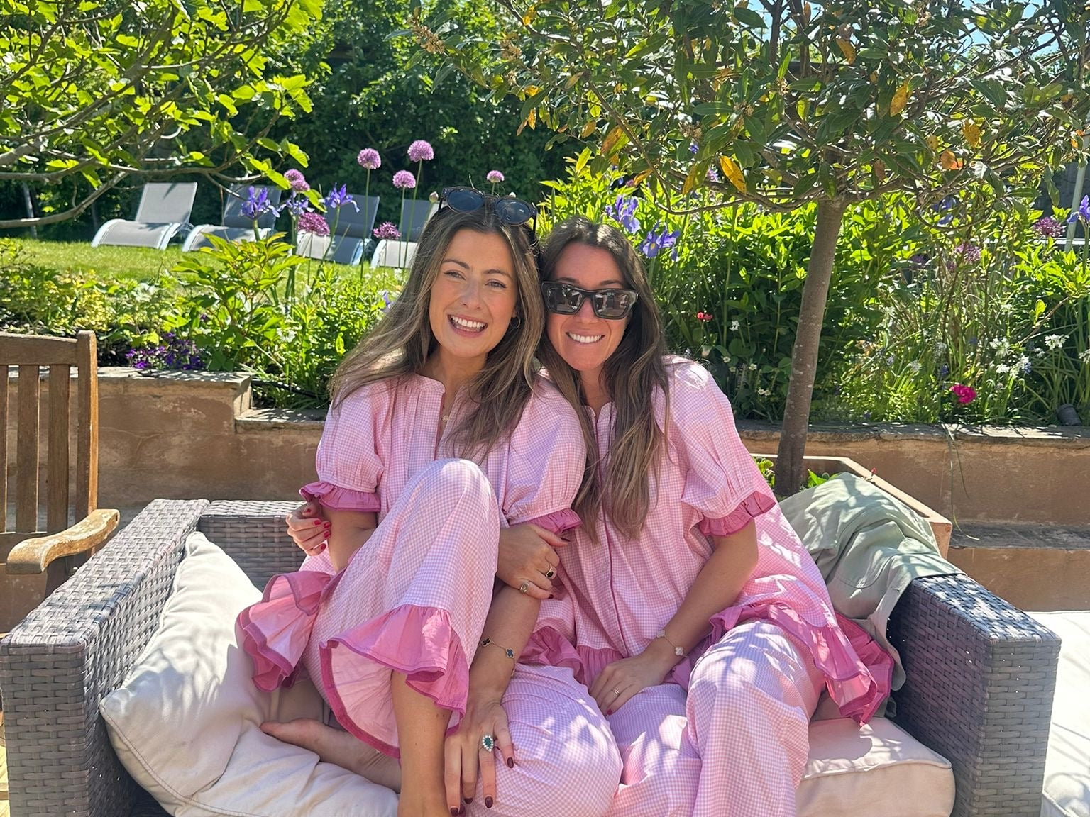Two women in pink robes sitting on a garden sofa with a garden background