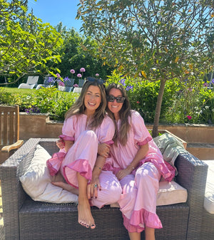 Two women in pink robes sitting on a garden sofa with a garden background