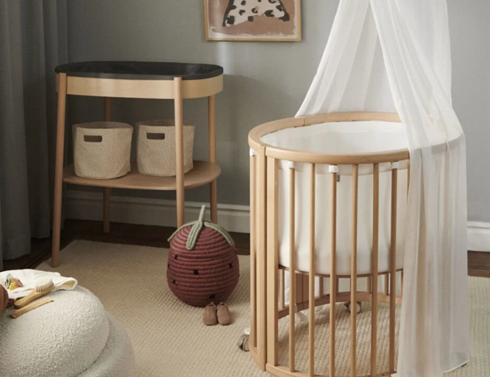 Stokke Sleepi Mini Bed Natural, bed with white canopy in a nursery beside a changing unit, rug and woven strawberry basket