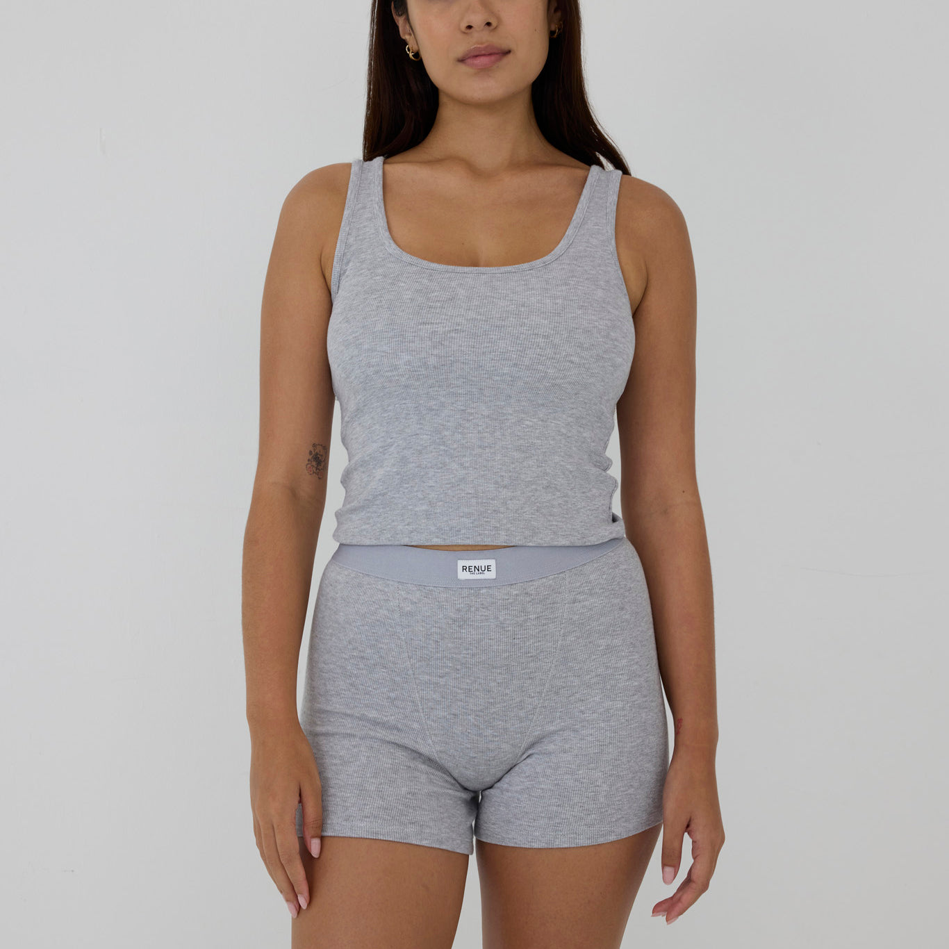 A woman modeling a light gray heathered two-piece loungewear set consisting of a scoop-neck tank top and matching high-waisted shorts with a visible PUMA logo on the waistband, set against a plain light gray background.
