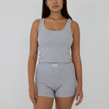 A woman modeling a light gray heathered two-piece loungewear set consisting of a scoop-neck tank top and matching high-waisted shorts with a visible PUMA logo on the waistband, set against a plain light gray background.