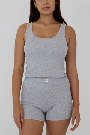 A woman modeling a light gray heathered two-piece loungewear set consisting of a scoop-neck tank top and matching high-waisted shorts with a visible PUMA logo on the waistband, set against a plain light gray background.