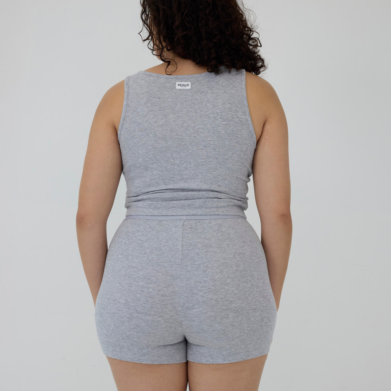 A woman shown from the back wearing a heather gray sleeveless tank top and matching high-waisted shorts against a plain light gray studio background.