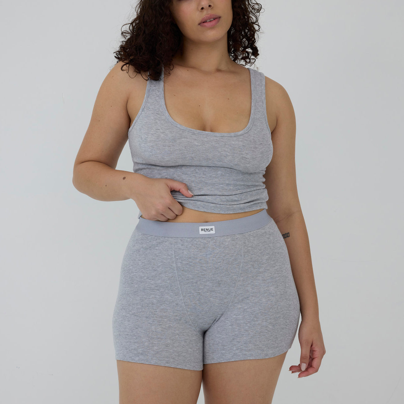 A woman modeling a light gray heathered two-piece activewear set consisting of a scoop-neck tank top and matching high-waisted shorts with a visible 'moult' brand label on the waistband, set against a plain light gray background.