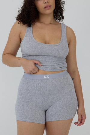 A woman modeling a light gray heathered two-piece activewear set consisting of a scoop-neck tank top and matching high-waisted shorts with a visible 'moult' brand label on the waistband, set against a plain light gray background.