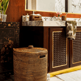 Handwoven Luxe Washing Hamper with its lid on, standing on a marble bathroom floor beside a basin unit