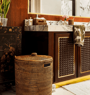 Handwoven Luxe Washing Hamper with its lid on, standing on a marble bathroom floor beside a basin unit
