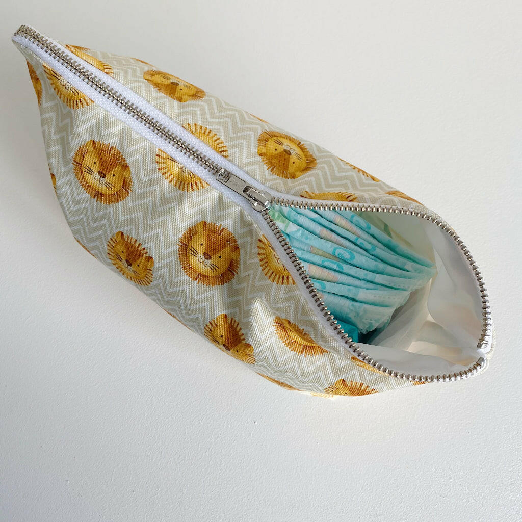 Nappy wallet in Leo lion print, partly unzipped at an angle with a stack of nappies showing through the opening