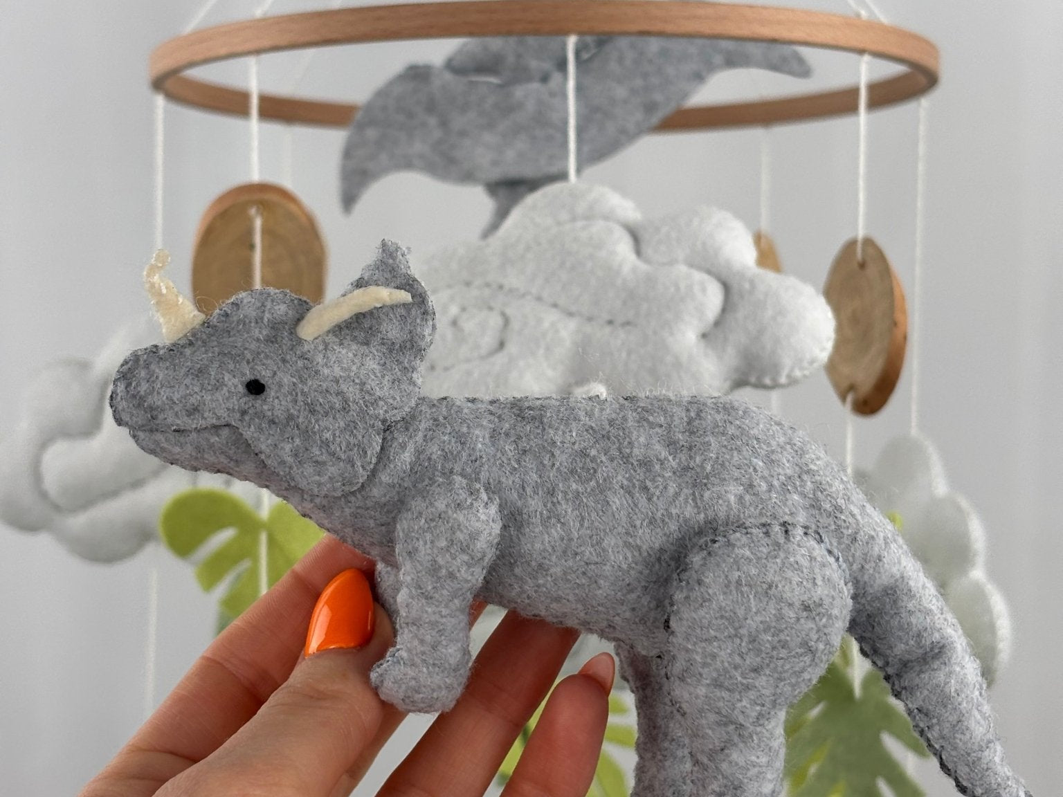 Little Dino Land felt cot mobile, hand holding the grey triceratops with cream horns, facing left