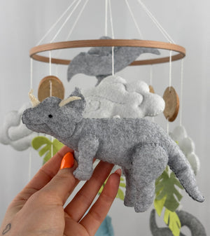 Little Dino Land felt cot mobile, hand holding the grey triceratops with cream horns, facing left