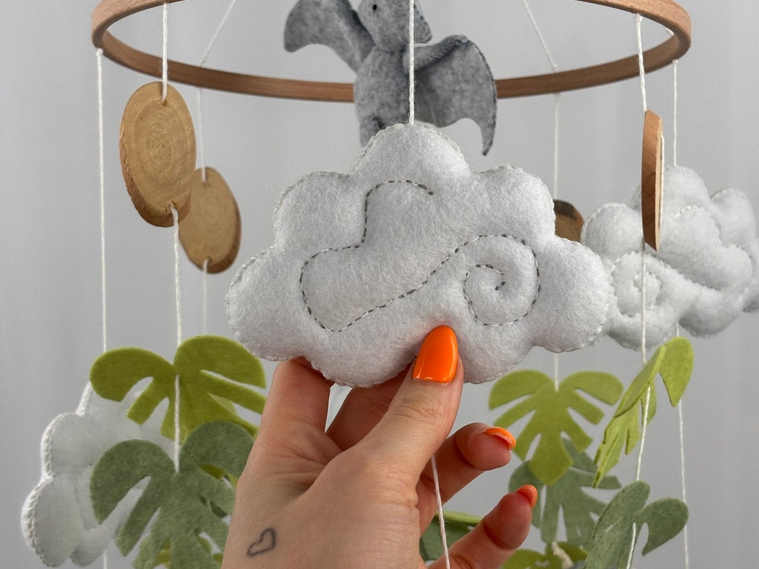 Little Dino Land felt cot mobile, hand holding a white felt cloud with grey swirl stitching