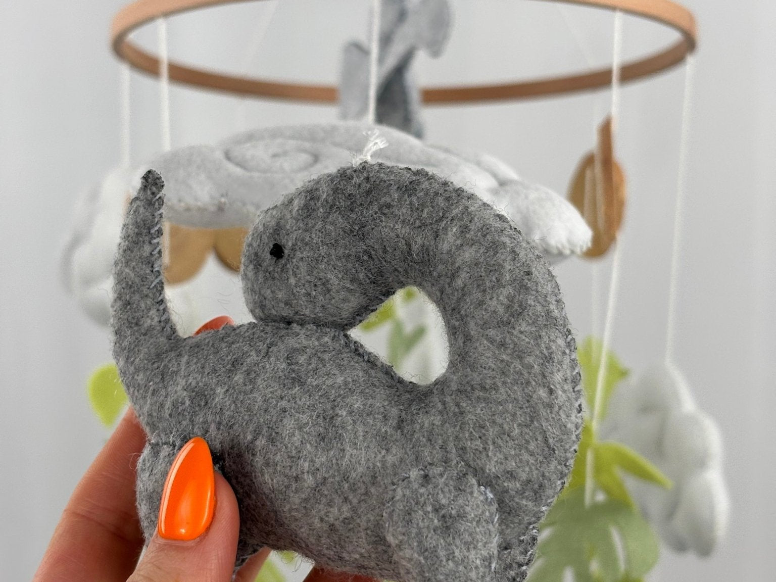 Little Dino Land felt cot mobile, hand holding the grey long-necked dinosaur from another angle, curved neck visible