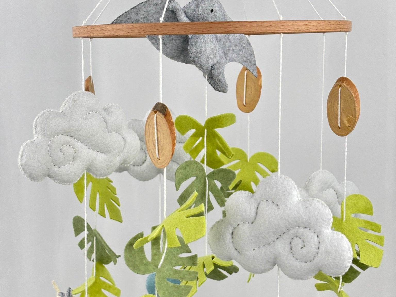 Little Dino Land felt cot mobile close-up of the upper ring, clouds, green leaves and wooden discs