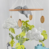 Little Dino Land felt cot mobile close-up of the upper ring, clouds, green leaves and wooden discs