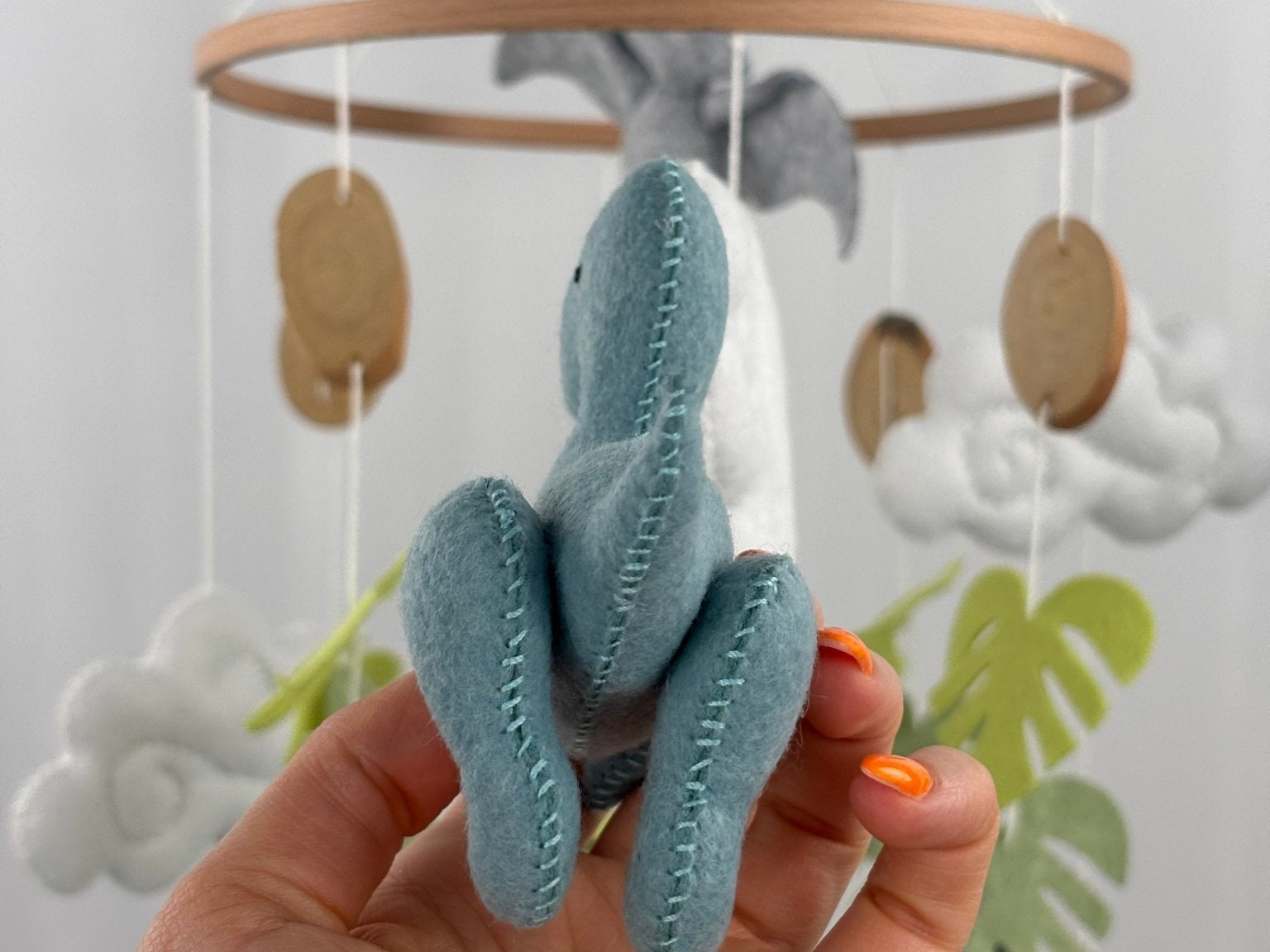 Little Dino Land felt cot mobile, hand holding the teal dinosaur from behind, showing stitched back legs