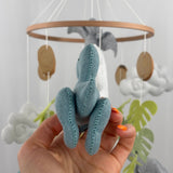 Little Dino Land felt cot mobile, hand holding the teal dinosaur from behind, showing stitched back legs