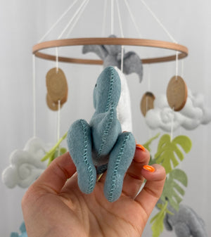 Little Dino Land felt cot mobile, hand holding the teal dinosaur from behind, showing stitched back legs