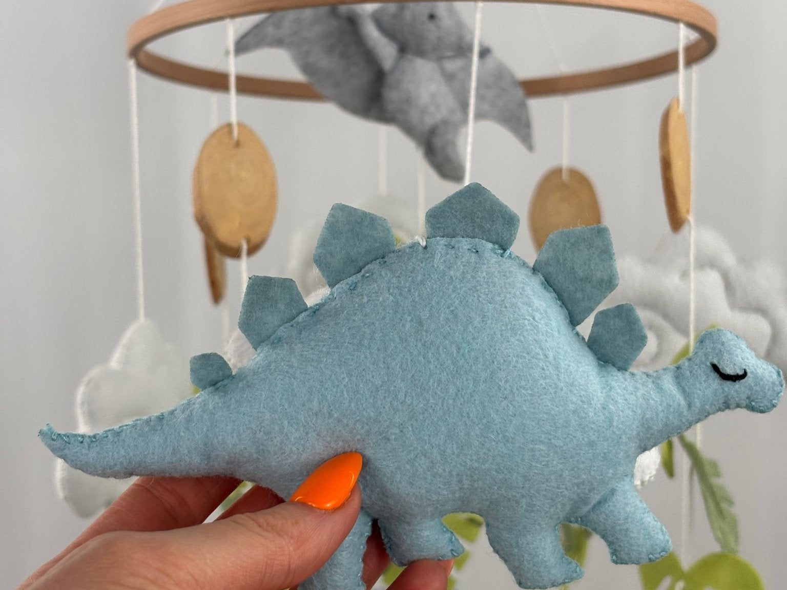 Little Dino Land felt cot mobile, hand holding the pale blue stegosaurus with a stitched edge and closed eye
