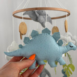 Little Dino Land felt cot mobile, hand holding the pale blue stegosaurus with a stitched edge and closed eye