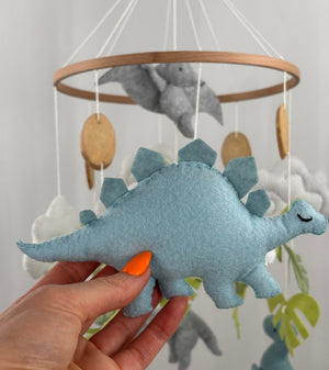 Little Dino Land felt cot mobile, hand holding the pale blue stegosaurus with a stitched edge and closed eye