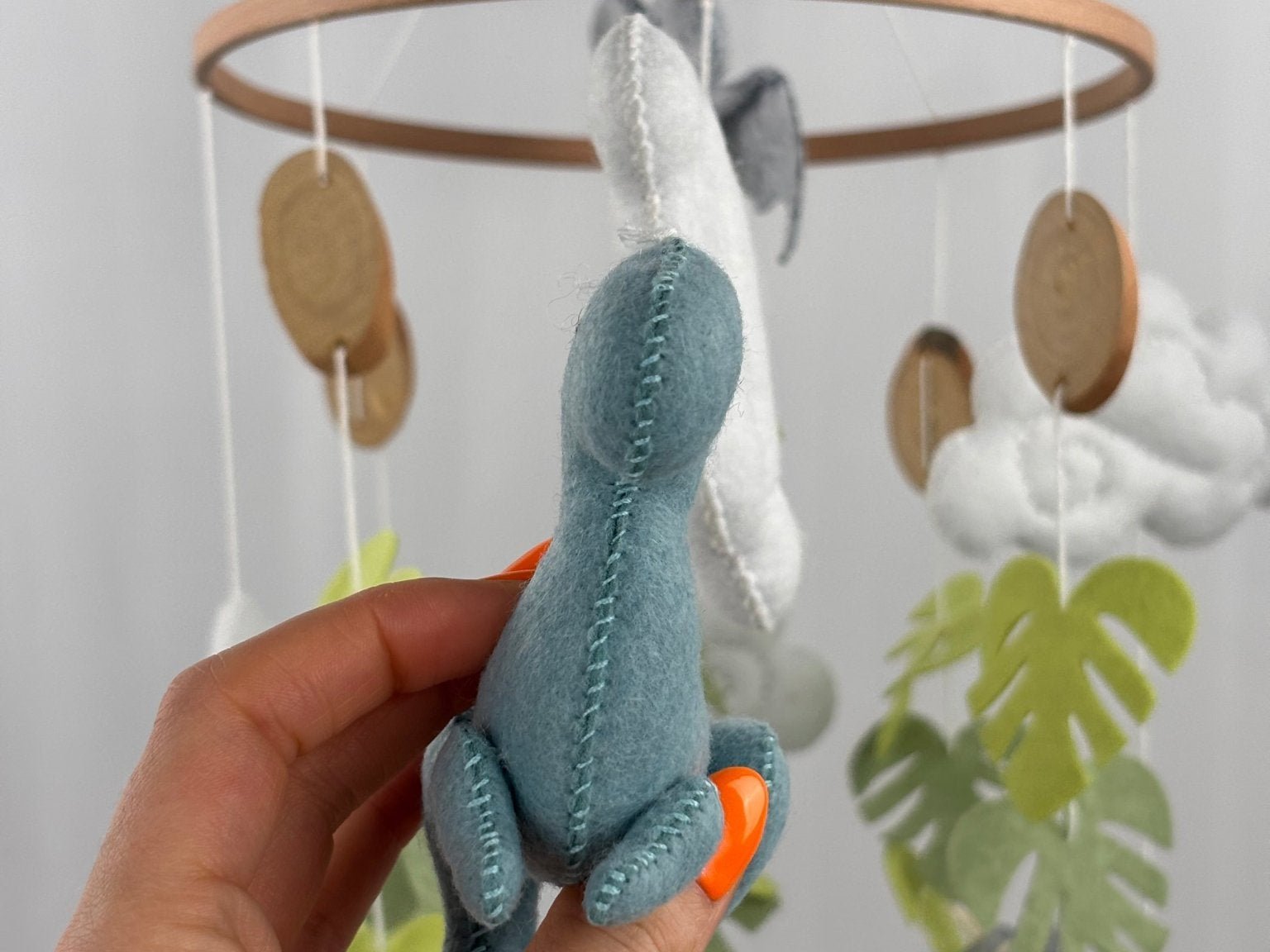 Little Dino Land felt cot mobile, hand holding the teal dinosaur from the front, showing the stitched seam