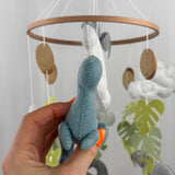 Little Dino Land felt cot mobile, hand holding the teal dinosaur from the front, showing the stitched seam