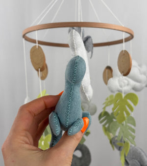 Little Dino Land felt cot mobile, hand holding the teal dinosaur from the front, showing the stitched seam