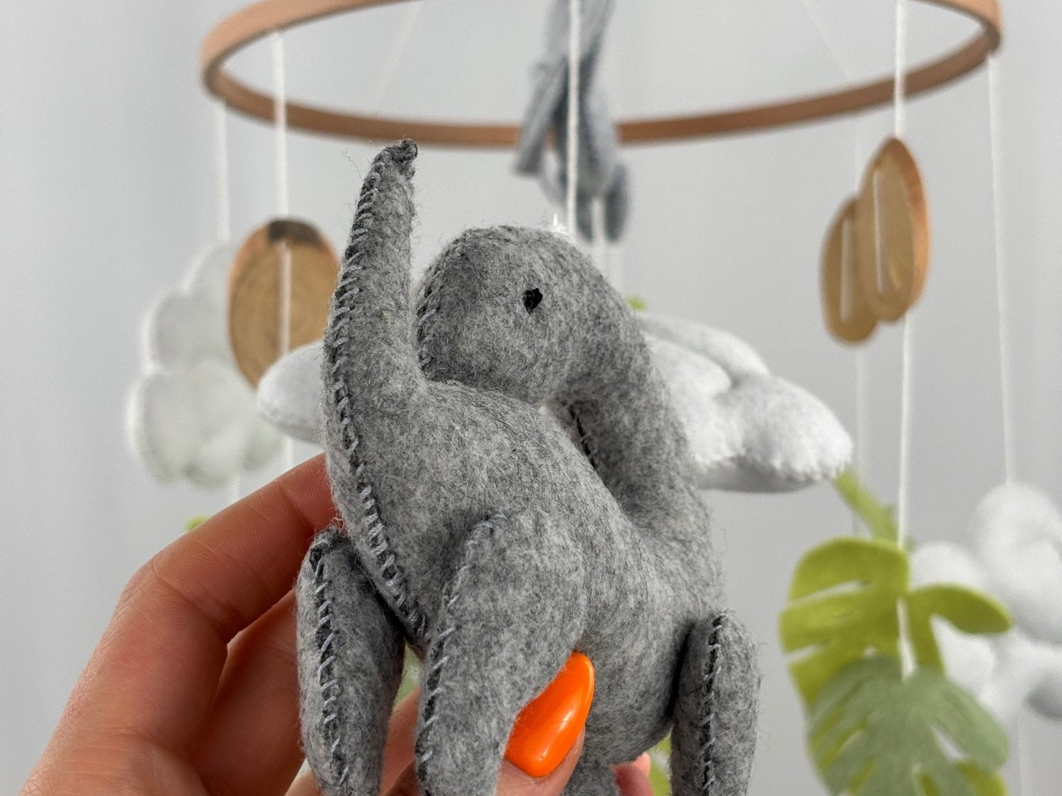 Little Dino Land felt cot mobile, hand holding the grey long-necked dinosaur, showing its side with stitched edges