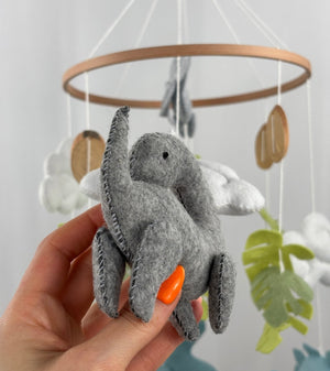 Little Dino Land felt cot mobile, hand holding the grey long-necked dinosaur, showing its side with stitched edges