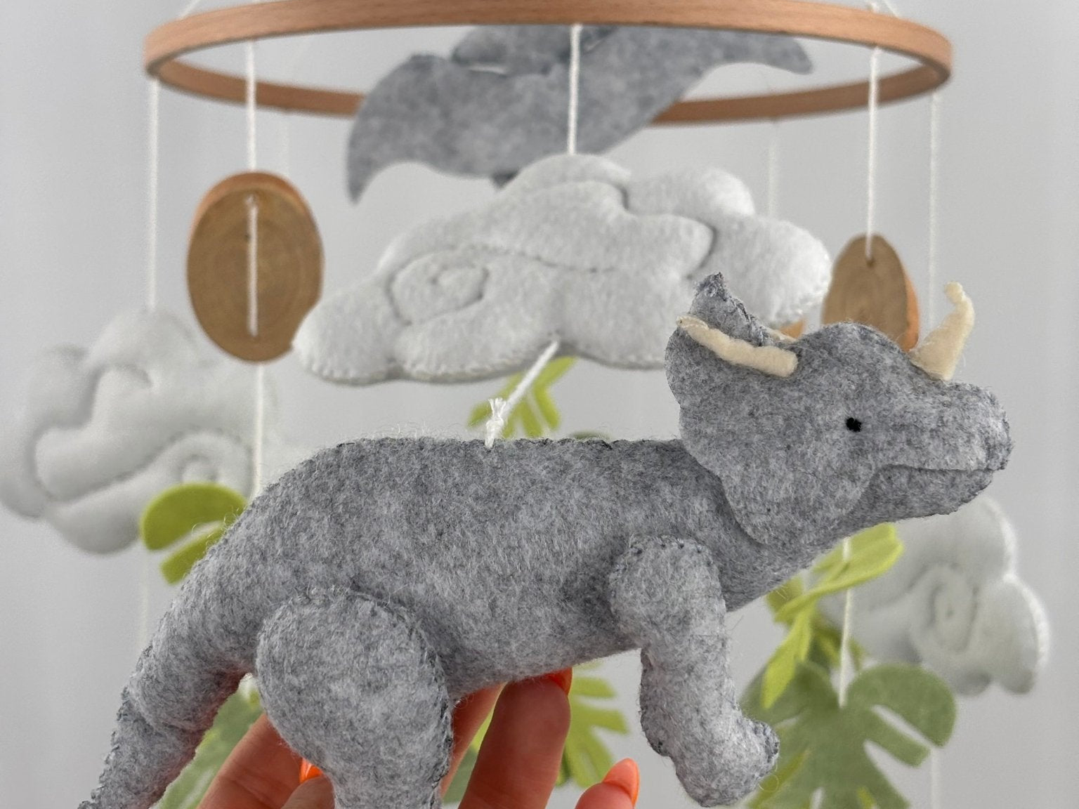 Little Dino Land felt cot mobile, hand holding the grey triceratops with cream horns, facing right