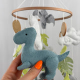 Little Dino Land felt cot mobile, hand holding the teal dinosaur in side view with a small black eye