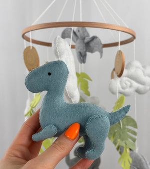Little Dino Land felt cot mobile, hand holding the teal dinosaur in side view with a small black eye