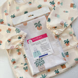 Splash Mat, Pot Plants: in its packaging laid on a matching plant print long-sleeved bib with elasticated cuffs