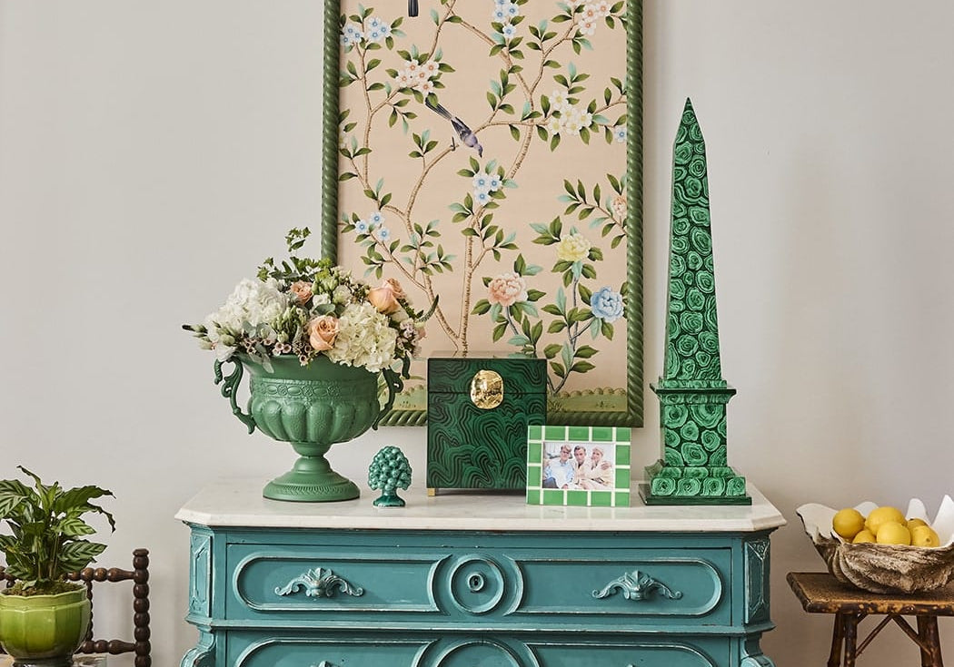 Mia Emerald Mosaic Photo Frame 6x4 on a teal chest of drawers with a green obelisk, urn of flowers and framed artwork