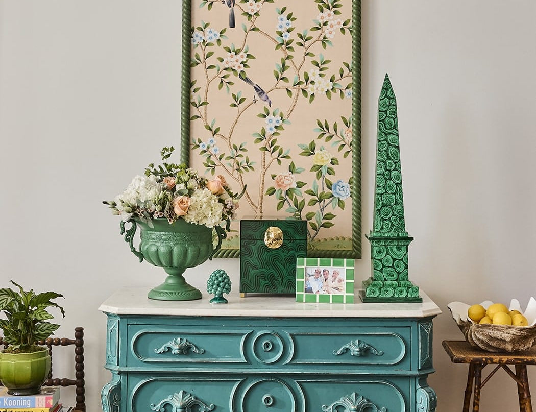 Mia Emerald Mosaic Photo Frame 6x4 on a teal chest of drawers with a green obelisk, urn of flowers and framed artwork