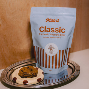 Milk it cookie dough bundle: blue Classic Oatmeal Chocolate Chip pouch on a tray beside a baked cookie on a spotted dish