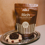 Milk it cookie dough bundle: brown Rich Triple Chocolate Chunk pouch on a tray beside a dark baked cookie on a spotted dish