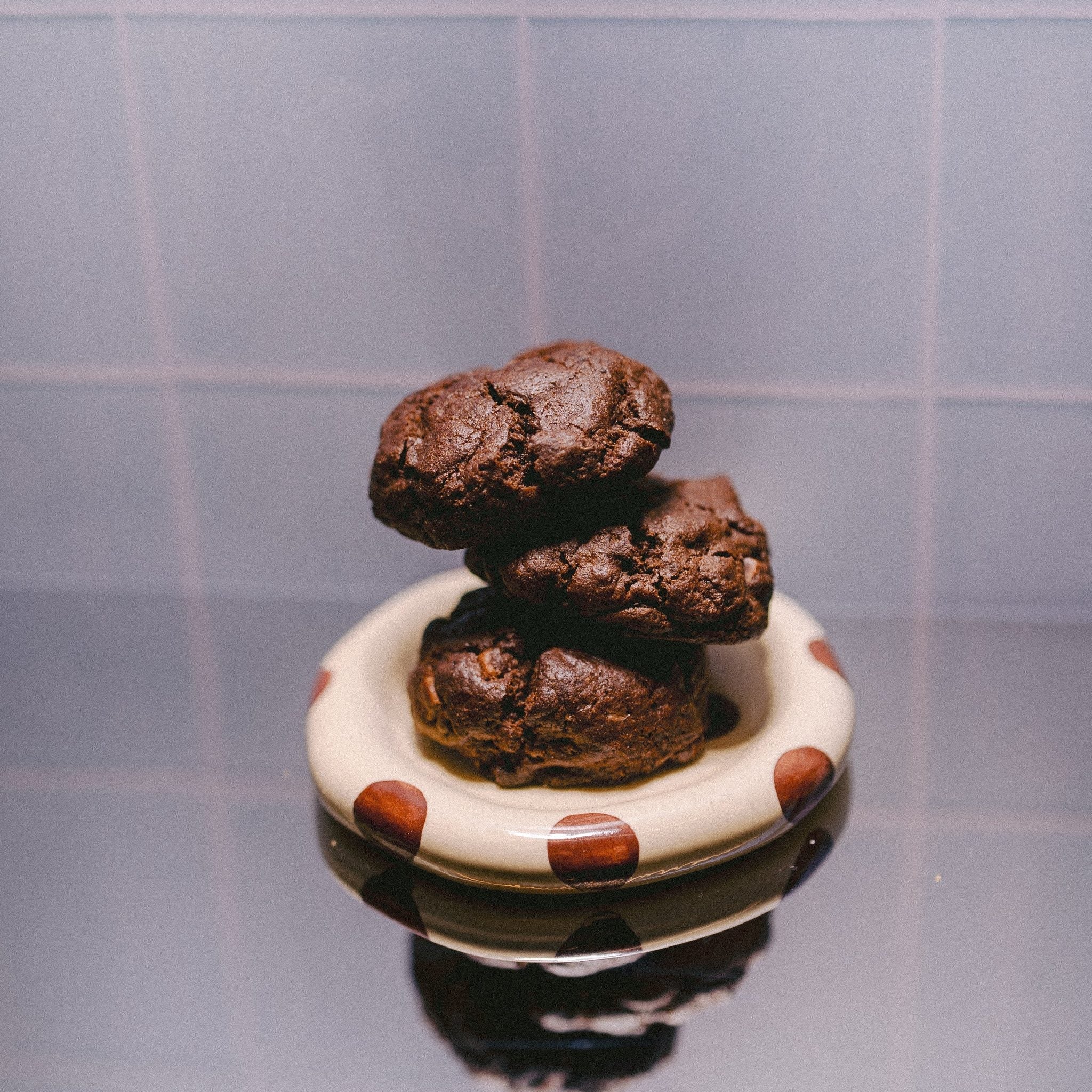 Milk it cookie dough bundle: stack of three baked dark chocolate cookies on a cream dish with brown spots